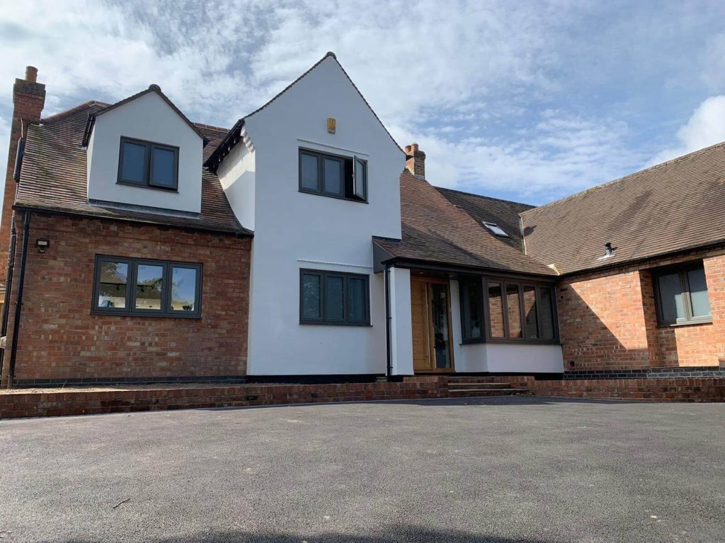 A modern detached house featuring a mix of white and red brickwork, grey-framed windows, and a spacious driveway.